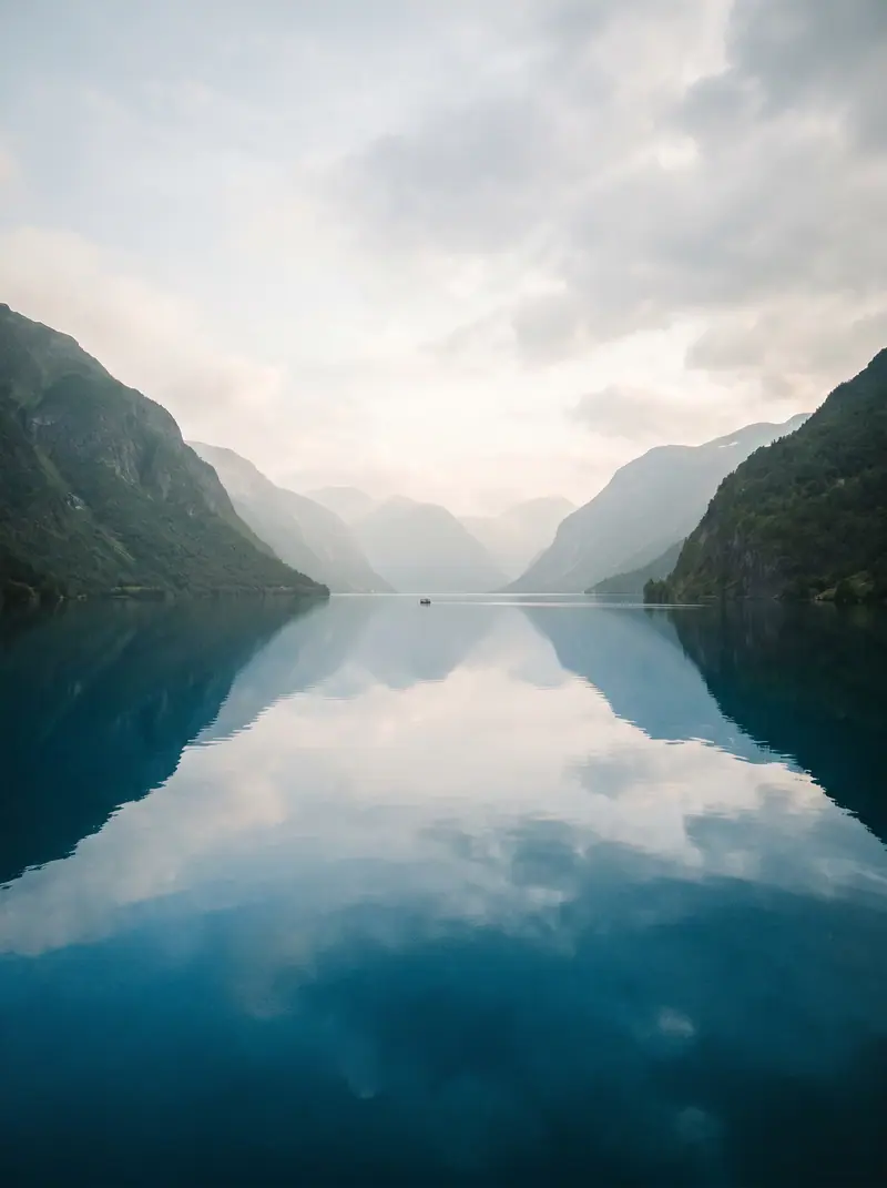 Fiordo en calma con reflejo del cielo entre montañas.
