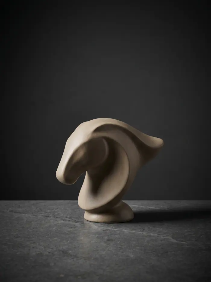 Escultura de arcilla abstracta de líneas fluidas sobre superficie de pizarra.